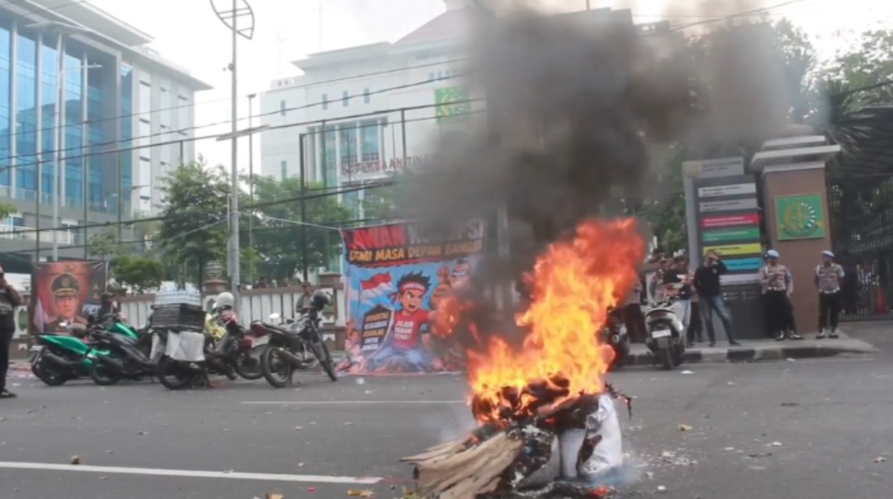 Massa AMI melakukan aksi bqkar spanduk dan kayu, sebagai bentuk protes atas penanganan kasus korupsi Eks Jampidsus Febrie Adriansyah di Kejati Jatim.