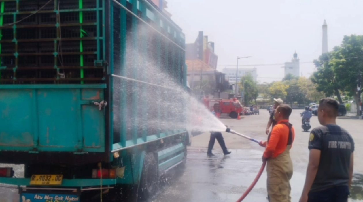 Petugas DPKP Surabaya menyemprotkan air ke truk pengangkut ayam untuk mencegah ayam kepanasan akibat suhu tinggi yang dipicu fenomena angin baratan.